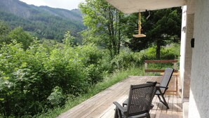 A wooden deck with two chairs facing a scenic view of a forested valley. - Spacious apartment with large terrace in nature (Allos)