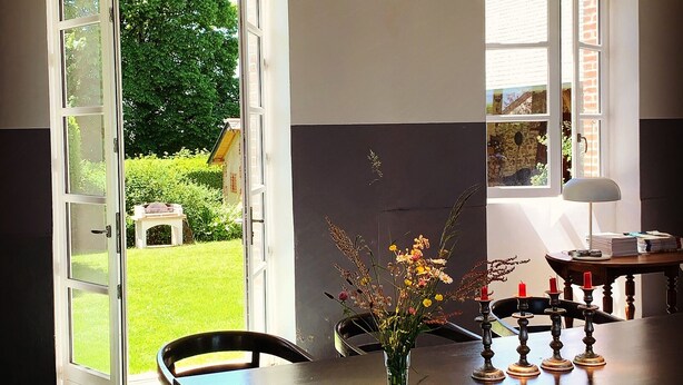 A dining area with a table, chairs, a vase of flowers, and a hanging light fixture. - Enjoy your holiday in a former school in the French Limousin (Troche)
