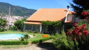 Ein Haus mit Ziegeldach, Schwimmbecken und einem Garten mit roten Blüten.