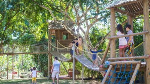 Une aire de jeux avec un pont de corde, des structures d’escalade et une maison de jeu en bois.
