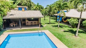 Une piscine dotée d’un patio couvert, entourée d’une végétation luxuriante et de palmiers.