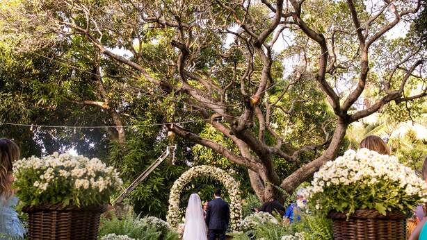 Une cérémonie de mariage où la mariée et le marié défilent le long d’un chemin bordé de paniers en osier remplis de fleurs.