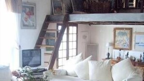 A cozy living room with a white sofa, a wooden coffee table, and a red patterned rug. There is a staircase leading to an upper level, and various decorative items are visible on shelves and tables. - Charming villa with swimming pool, Avignon, 6 people, large Mediterranean garden (Villeneuve-Lès-Avignon)