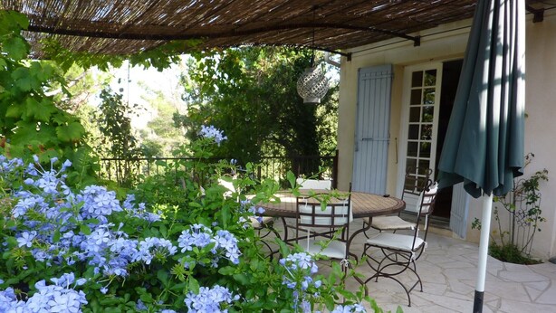 An outdoor patio with a round table and chairs, surrounded by lush greenery and flowering plants. - Charming villa with swimming pool, Avignon, 6 people, large Mediterranean garden (Villeneuve-Lès-Avignon)
