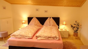 A bedroom with a wooden ceiling, two bedside tables with lamps, a bed with floral bedding, a radiator, and a potted plant. - Vacation apartment in Hochkönig, hiking possibilities just in front of the door (Mühlbach/Hochkönig)