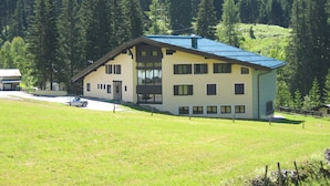A two-story building with a sloped roof, large windows, and a grassy yard. - Vacation apartment in Hochkönig, hiking possibilities just in front of the door (Mühlbach/Hochkönig)