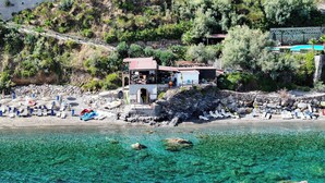 Un hôtel situé sur la côte, avec une plage, une eau cristalline et un paysage rocheux.