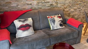 Ein modernes Wohnzimmer mit grauem Sofa, Zierkissen, einer roten Tagesdecke und einem Couchtisch mit roter Ablagefläche.