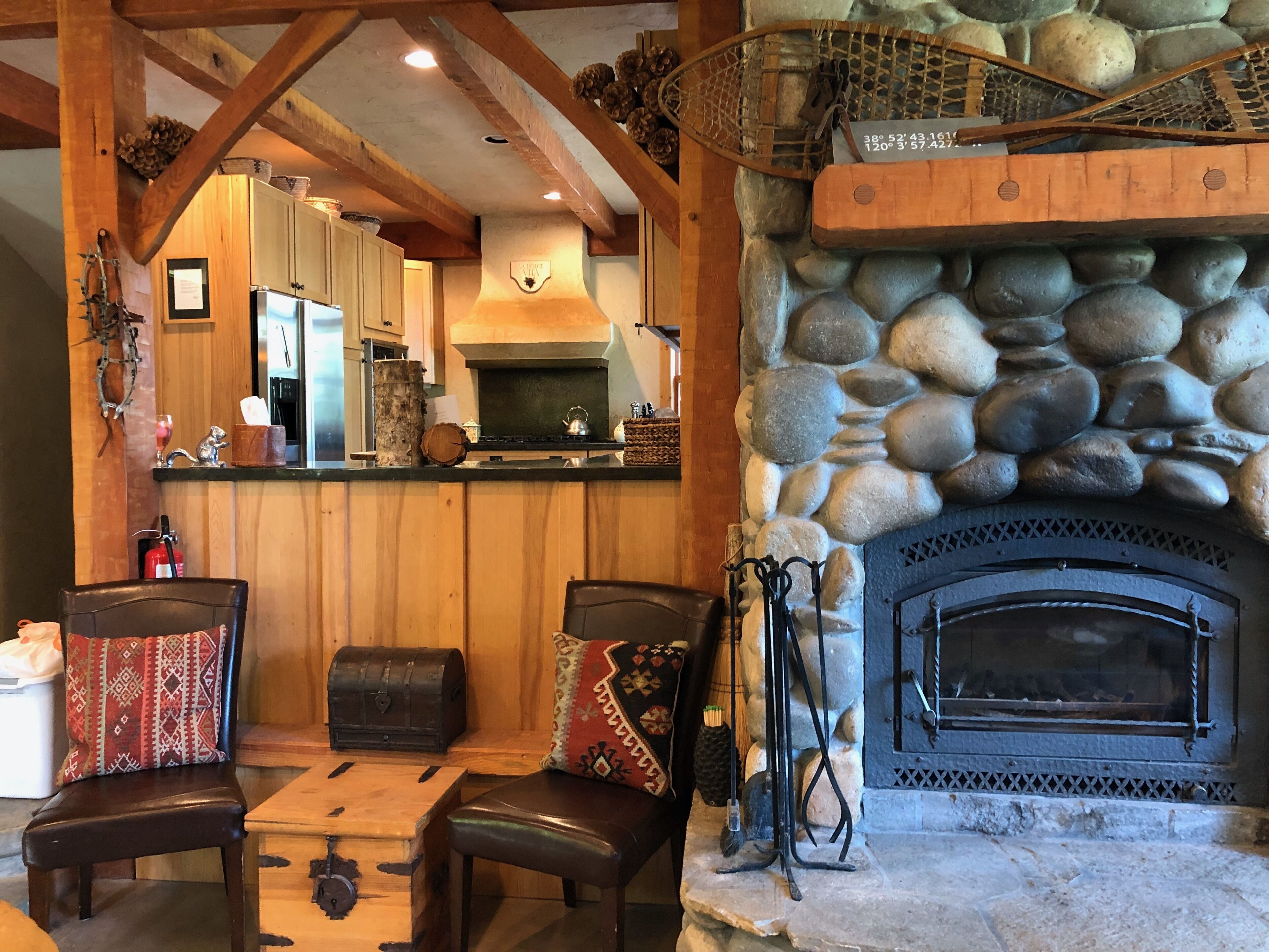 A rustic interior with a stone fireplace, wooden beams, and a cozy seating area with a table and chairs.