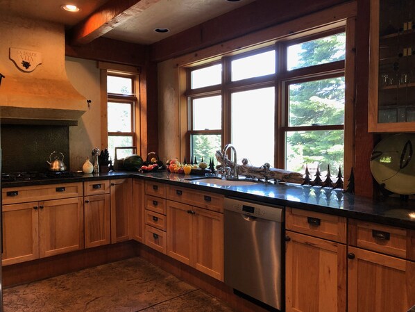 A kitchen with wooden cabinets, a stainless steel dishwasher, and a large window with a view of trees.