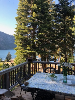 A deck with a table and chairs, overlooking a lake and forested hills.