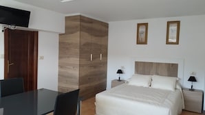 Ein Schlafzimmer mit Bett, Nachttischen, einem an der Wand befestigten Fernseher und einem Kleiderschrank.