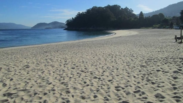 Ein Sandstrand mit freiem Blick auf das Meer und entfernte Berge.