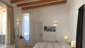 A bedroom with a bed, a dresser, a mirror, a window with curtains, a radiator, a lamp, and a picture on the wall.