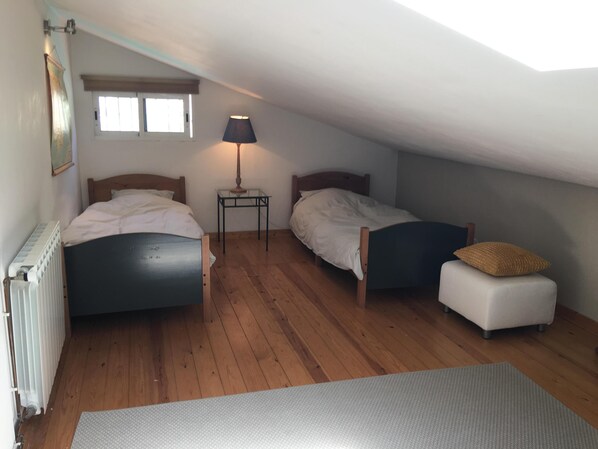 A small, cozy attic bedroom with two beds, a nightstand, a lamp, and a radiator.