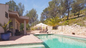 A swimming pool with clear water, surrounded by a stone wall and a covered seating area with umbrellas.