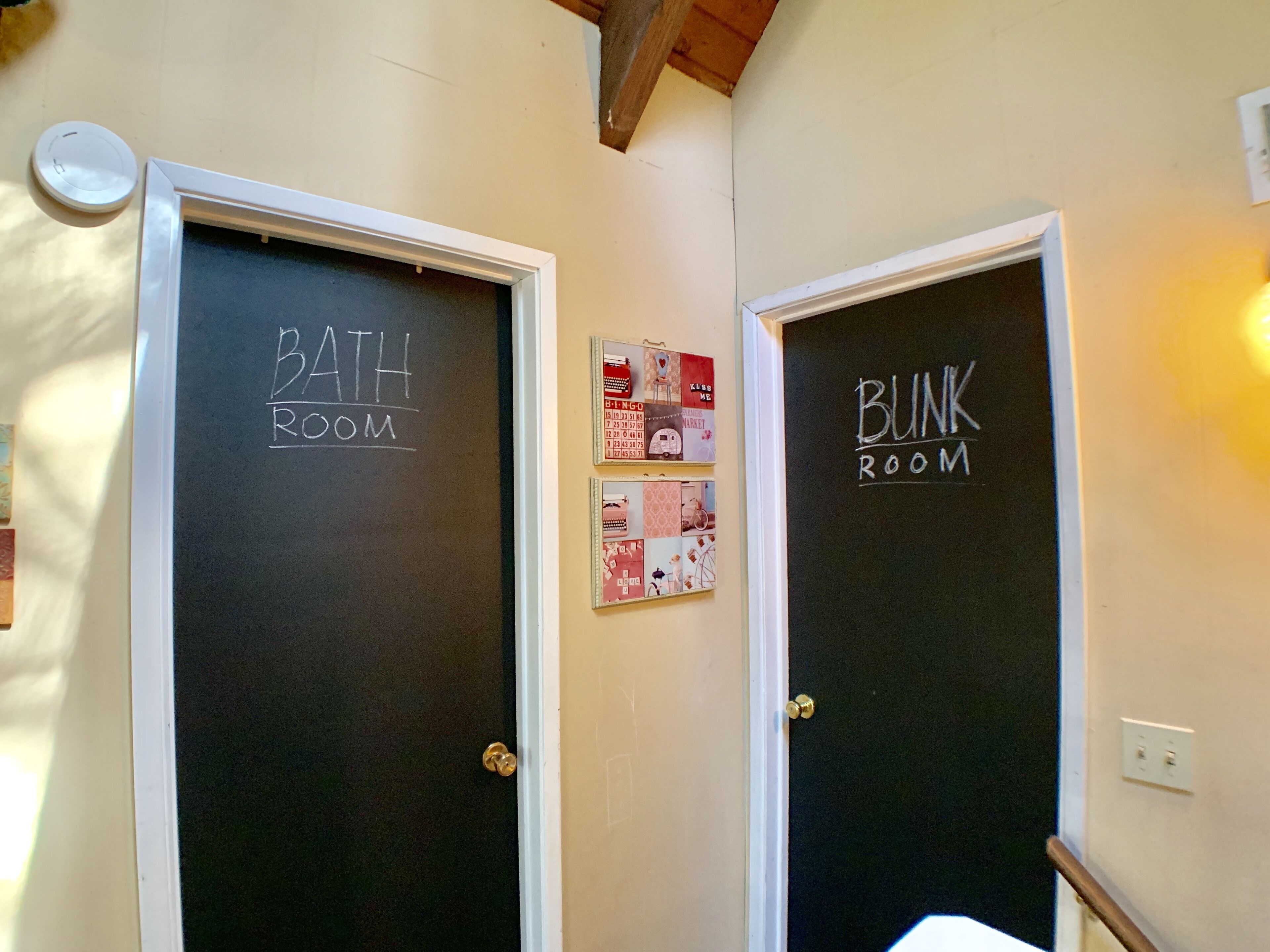 Due porte con le scritte 'BATH ROOM' e 'BUNK ROOM', con una piccola galleria fotografica appesa al muro tra di esse.