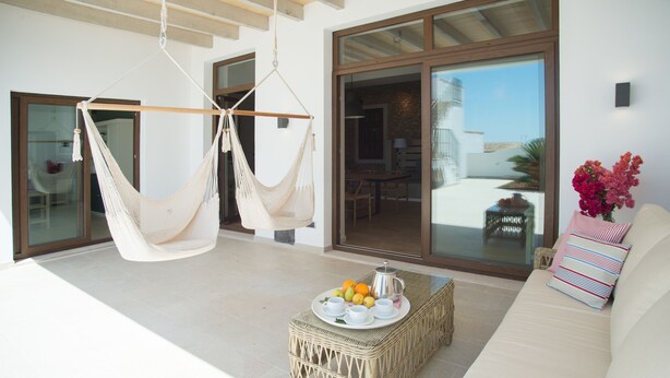 A modern living room with a hammock, a wicker coffee table with fruit and a coffee pot, and a sofa with striped pillows. - Ferrer de Shorta Modern holiday home for 10, private pool, A/C and Wi-Fi (S'Horta)