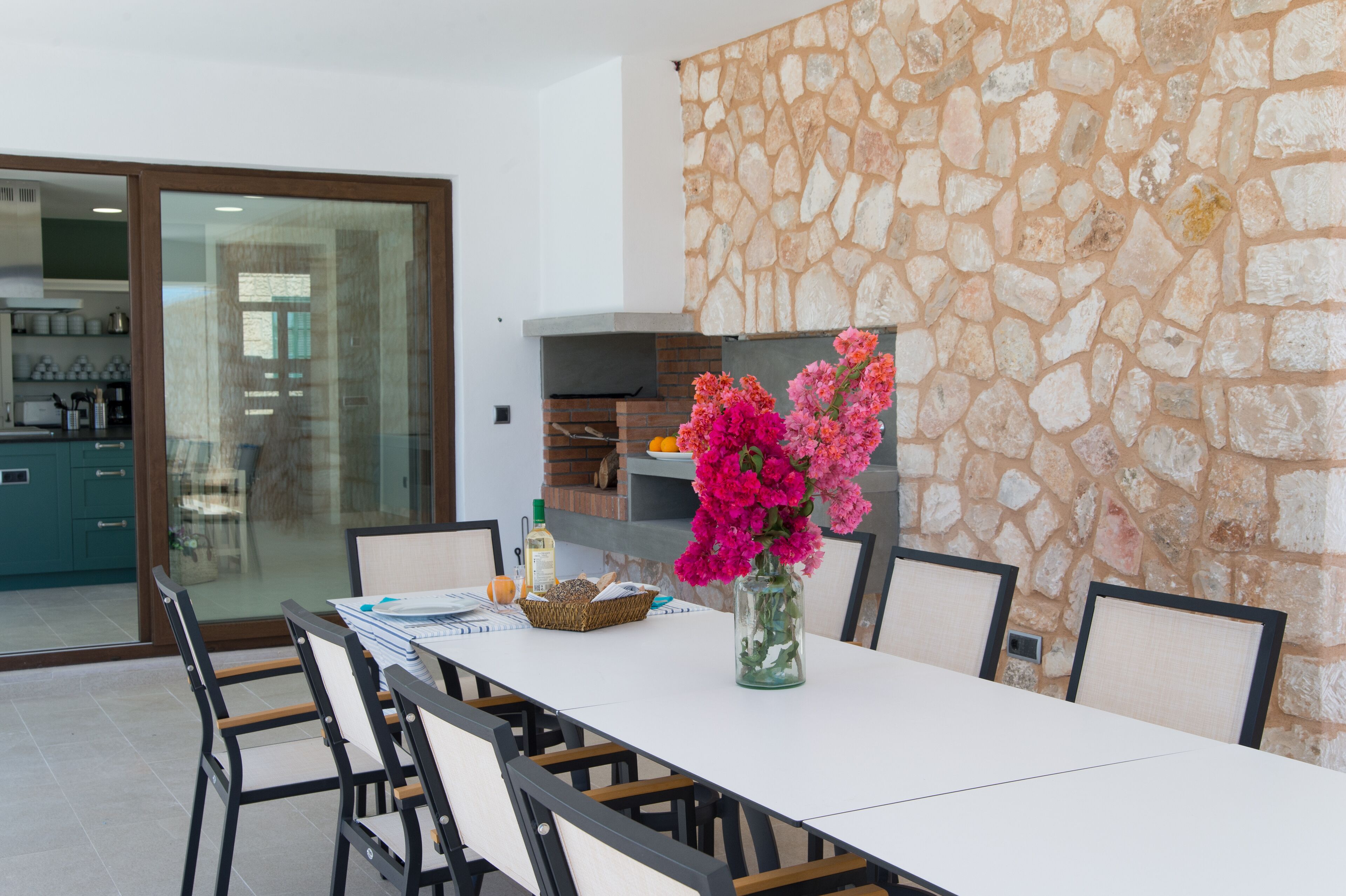 Un coin repas avec un mur en pierre, une porte vitrée donnant sur la cuisine et un vase rempli de fleurs placé sur la table.