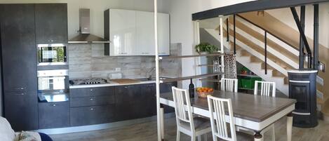 A modern kitchen with dark cabinetry, a built-in oven, and a dining area with a table and chairs.