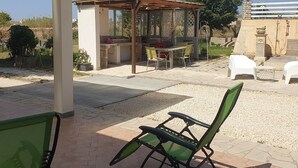 Un'area patio con una pergola, posti a sedere all'aperto e una piccola struttura coperta.