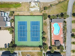 Vue aérienne d’une propriété comprenant deux courts de tennis, une piscine et de nombreux espaces verts.