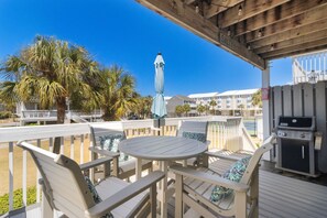 Un espacio de estar al aire libre con techo, una parrilla, muebles blancos y vistas a la playa y edificios.