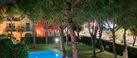 A swimming pool surrounded by trees and a building with illuminated windows.