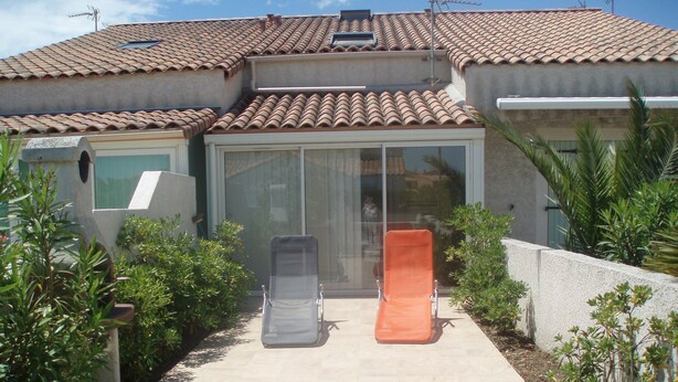 Een huis met een pannendak, een glazen deur en twee buitenstoelen.