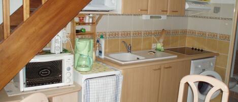 Een kleine keuken met een magnetron, koffiezetapparaat, spoelbak en houten kastjes.