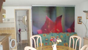 Een eethoek met een ronde tafel, stoelen en een vaas met bloemen. Achter de tafel hangt een groot schilderij aan de muur.