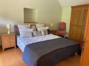 Ein Schlafzimmer mit einem Bett, zwei Nachttischen, einem Sessel, einem Kleiderschrank und einem Spiegel.