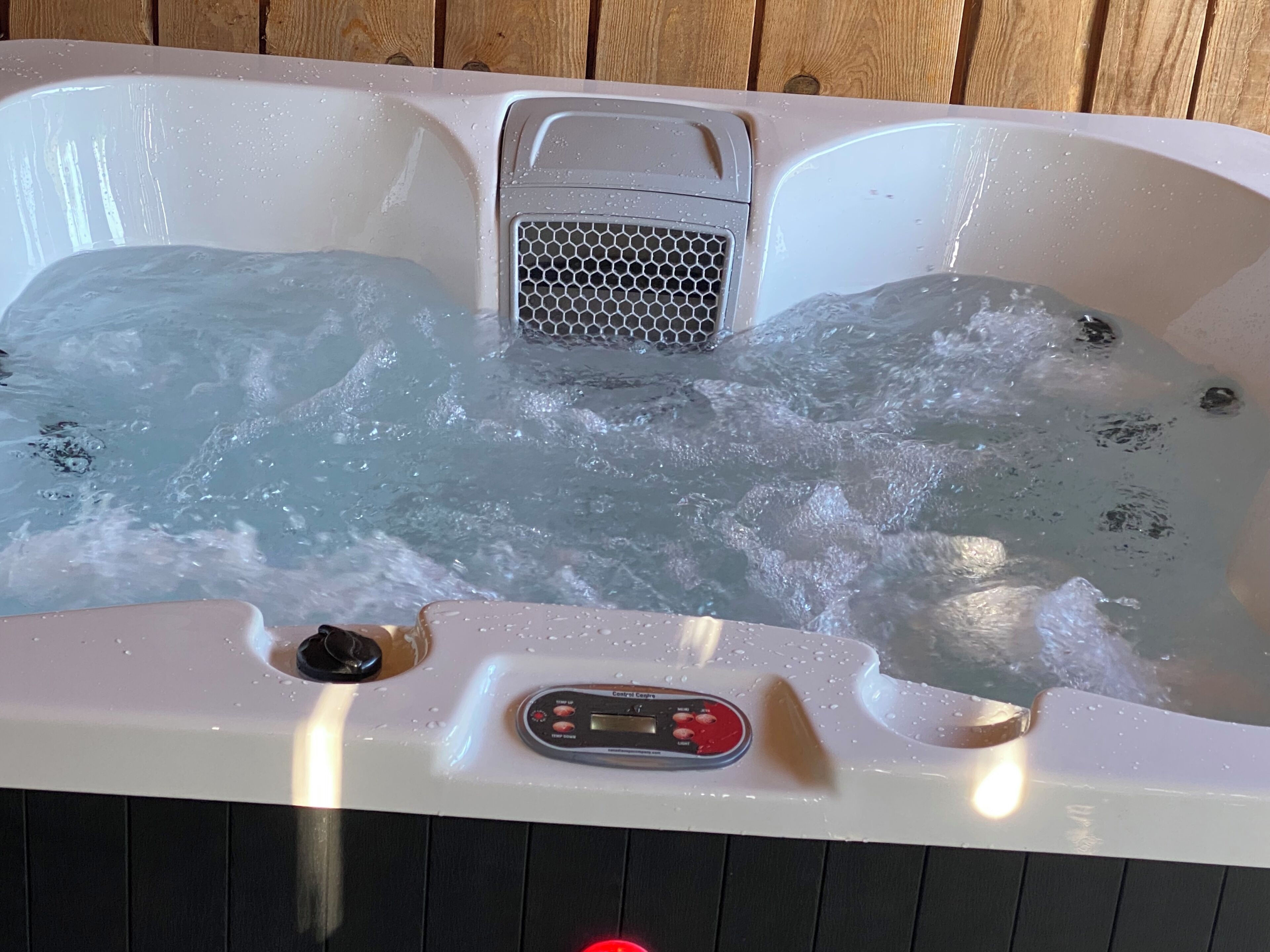 A hot tub with a control panel, a mesh drain, and a wooden deck in the background.