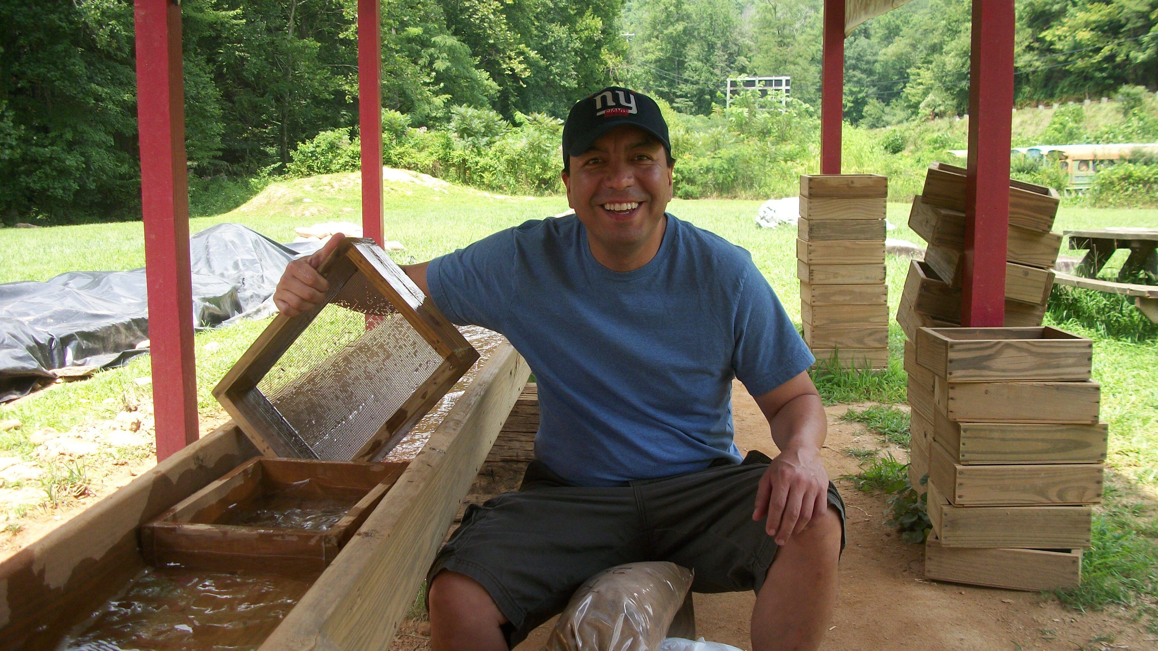 A person sitting under a wooden structure with a wooden trough in front of them.