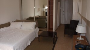 Hotellihuone, jossa on sänky, työpöytä lampun kanssa, tuoli, vaatekaappi ja peili.