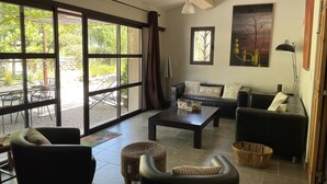 A spacious living area with a large sliding glass door leading to an outdoor patio, a leather sofa, a coffee table, and a wicker ottoman.