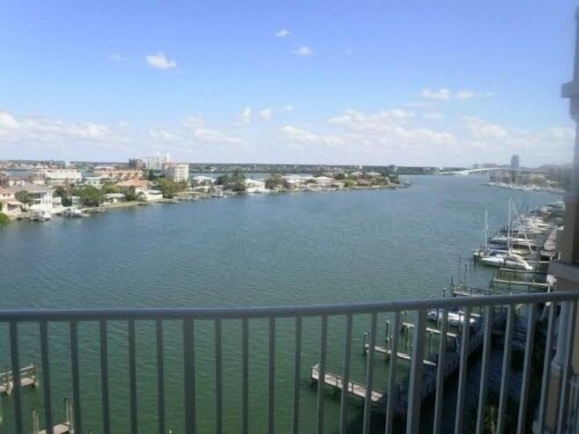 A marina with boats docked, a bridge in the background, and buildings along the waterfront.