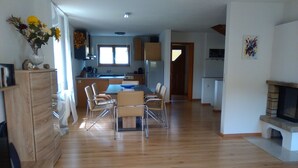 A spacious living area with a wooden floor, a dining table with chairs, a kitchen area with cabinets, and a fireplace. - House right on the edge of the forest, right at the foot of the Black Forest  (Schopfeim Ortsteil Enkenstein)