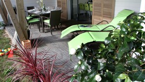 Un espace patio comprenant une table à manger pour quatre personnes, entourée de chaises, et un coin salon avec des coussins verts.