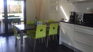 Une cuisine moderne avec un coin repas, dotée d’un plan de travail foncé, de chaises vertes et d’une machine à café.