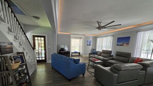 A spacious living room with a large blue sofa, a grey sectional, and a ceiling fan. - Relax in your home; yards from the Frankfort Beach and the downtown attractions. (Frankfort)