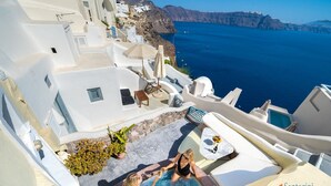 Un edificio de paredes blancas con piscina, mobiliario exterior y vistas al mar.