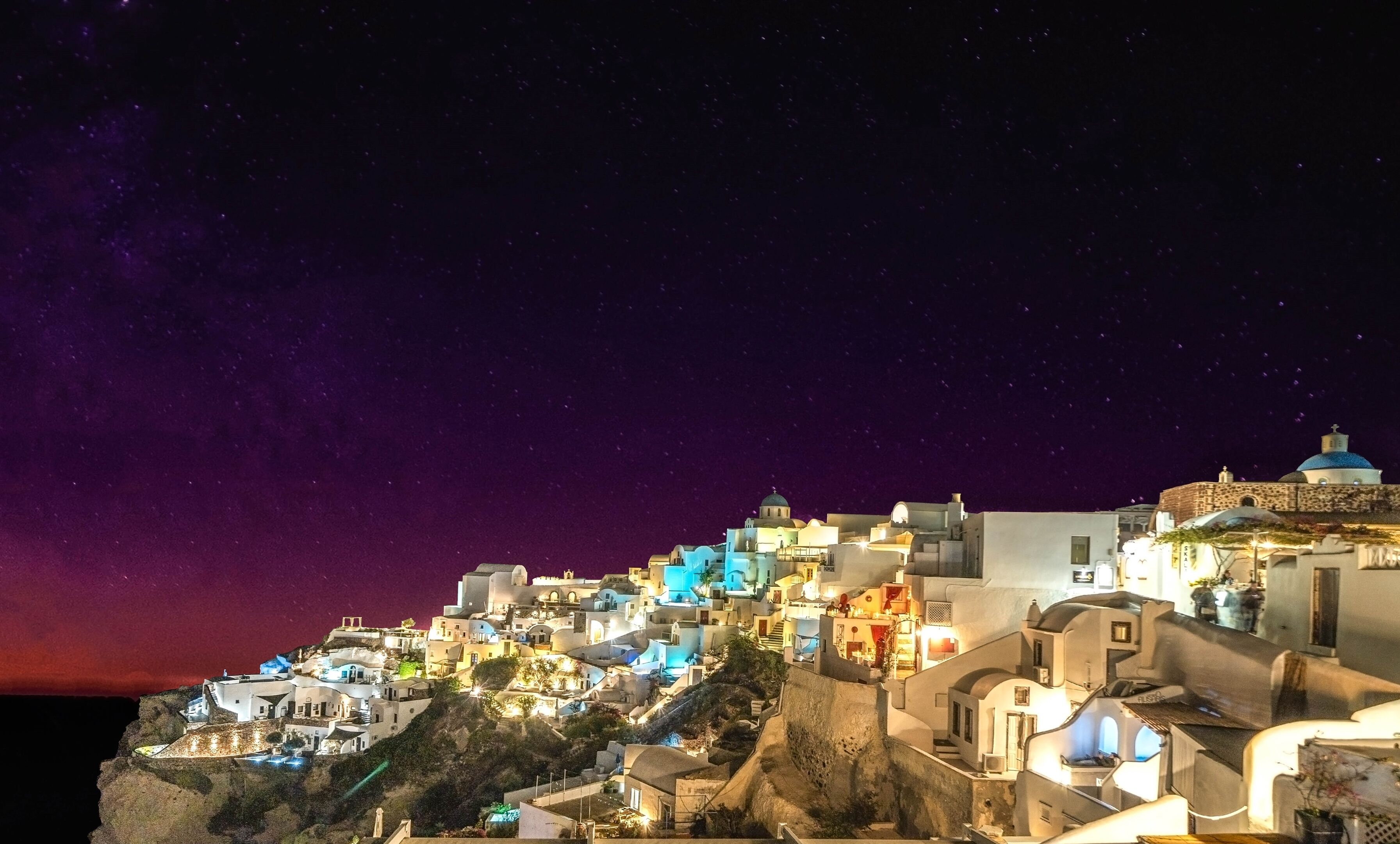 A coastal village with white buildings, steep terrain, and a starry night sky.