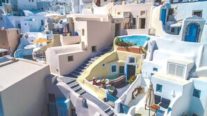 Un edificio blanco con detalles azules, una escalera que lleva a una terraza en la azotea y un área de estar al aire libre.