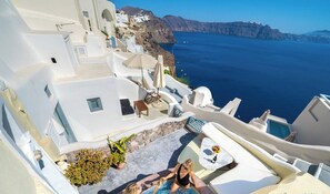 A white-walled building with a pool, outdoor seating, and a view of the sea. - SantoriniParadise: PARADISE cave house, indoor winery & outdoor hot tub, Caldera (santorini)