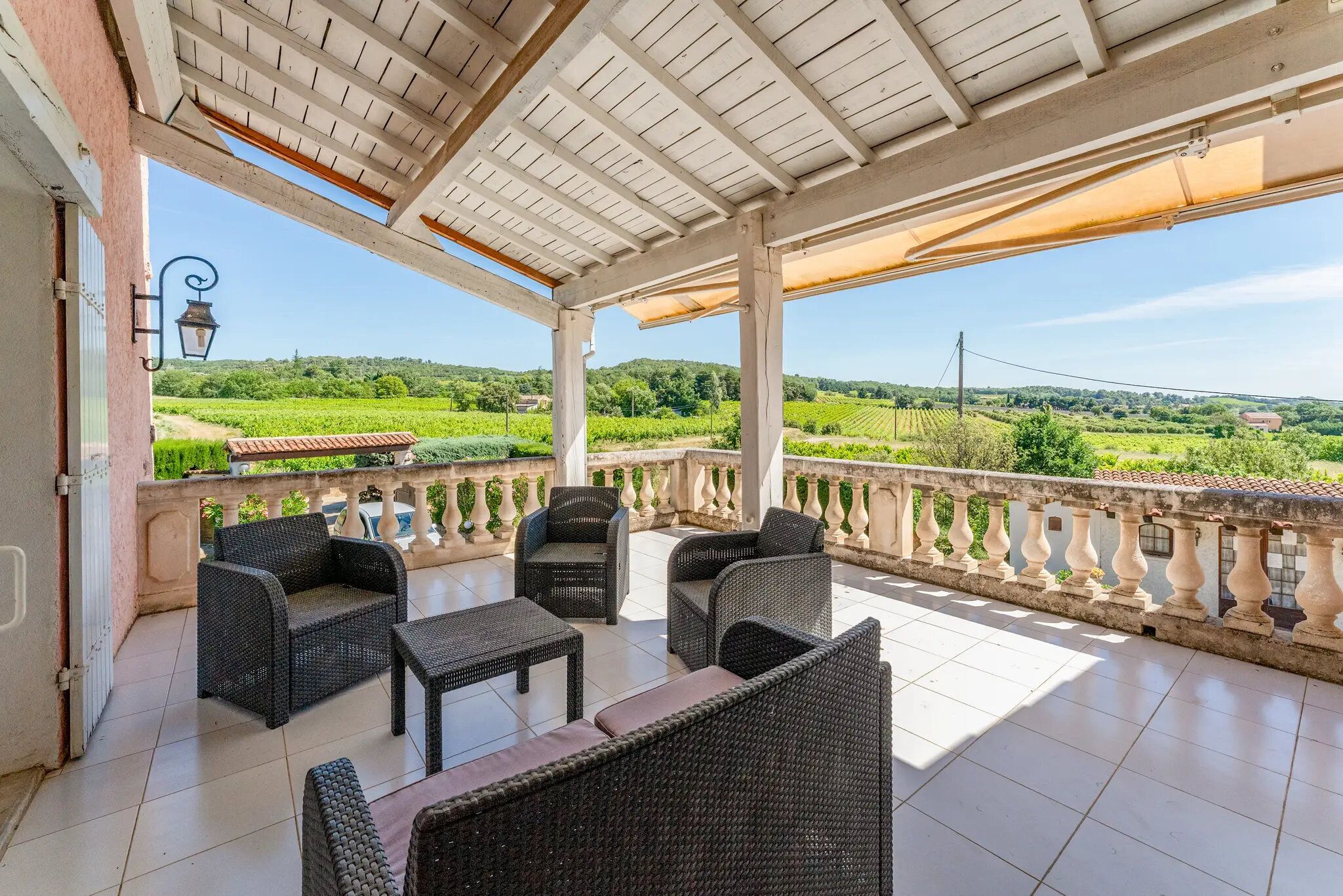 Un espace extérieur aménagé, abrité et doté de meubles en osier, d’un sol carrelé et offrant une vue sur un vignoble.