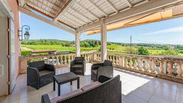 Un espace extérieur aménagé, abrité et doté de meubles en osier, d’un sol carrelé et offrant une vue sur un vignoble.