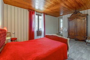Ein Zimmer mit einem großen Bett, einem Holzschrank, einem Sessel und einem Schreibtisch mit einer Lampe.