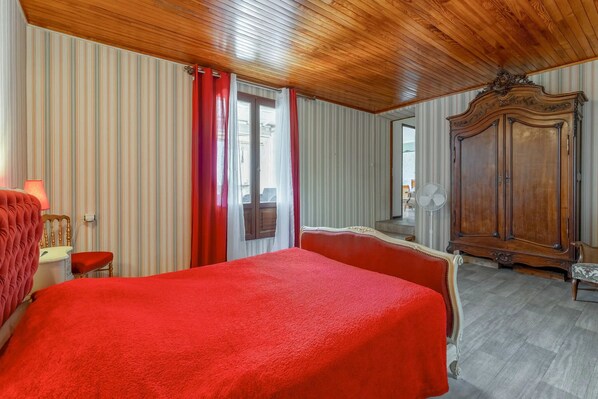 Ein Zimmer mit einem großen Bett, einem Holzschrank, einem Sessel und einem Schreibtisch mit einer Lampe.