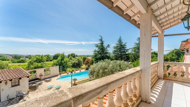 Un balcon avec vue sur une piscine, du mobilier d’extérieur et une pergola.